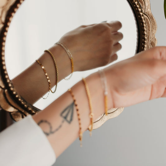 Close-up of hands with gold bracelets and a tattoo on a neutral background