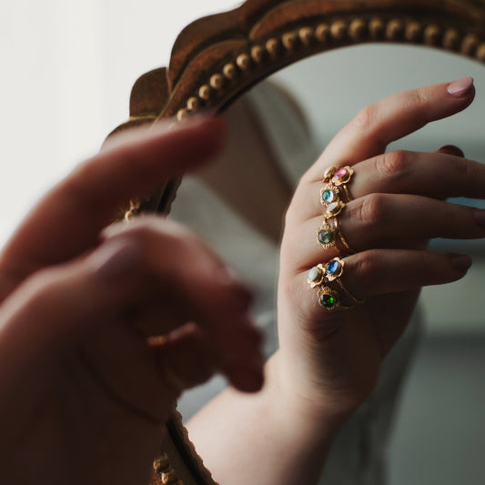 Hand with multiple rings in front of a decorative mirror