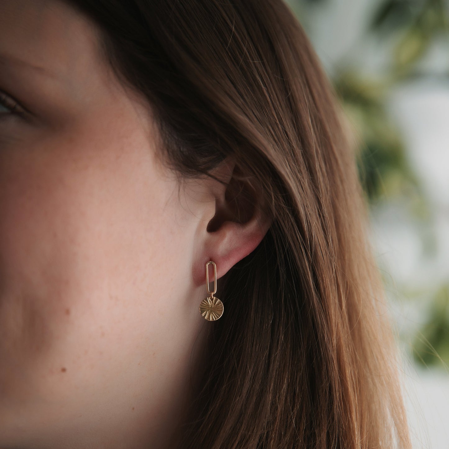 Close-up of a person wearing gold hoop earrings with a blurred background