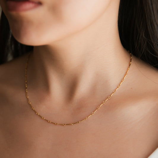 A gold bar link necklace being worn by a person.
