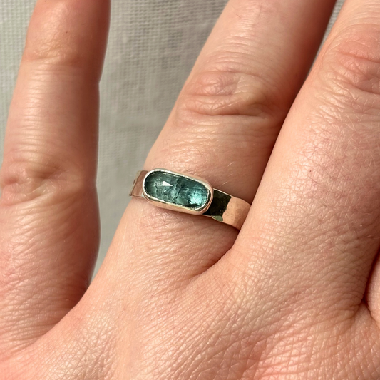 Silver ring with a blue gemstone on a person's finger against a neutral background