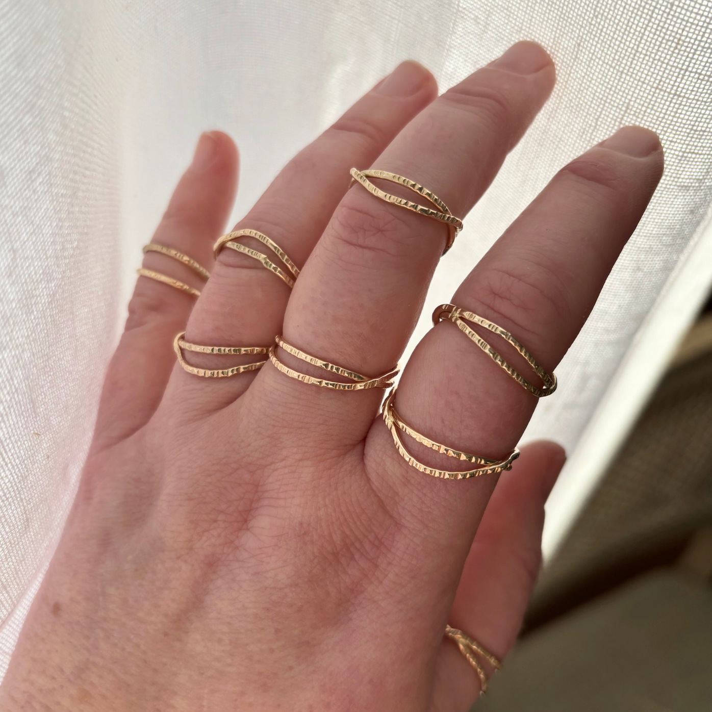 Hand wearing multiple gold rings on a neutral background