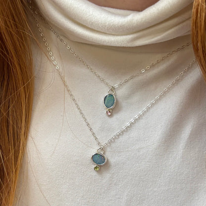 Two silver necklaces with gemstone pendants on a white turtleneck.