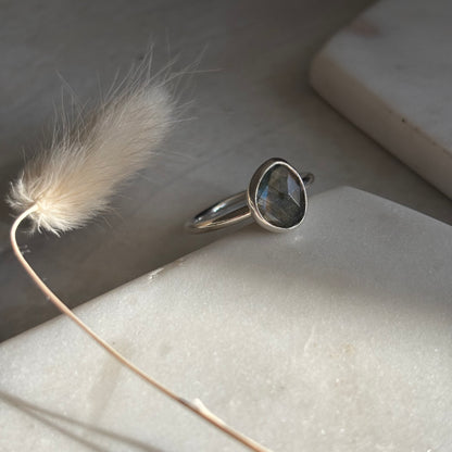 Silver ring with a gemstone on a marble surface with a feather
