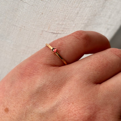 Gold ring with a pink gemstone on a person's finger against a neutral background