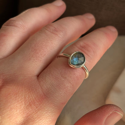 Hand wearing a ring with a blue gemstone on a blurred background