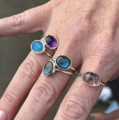 Close-up of a hand wearing five silver rings with gemstones against a blurred natural background