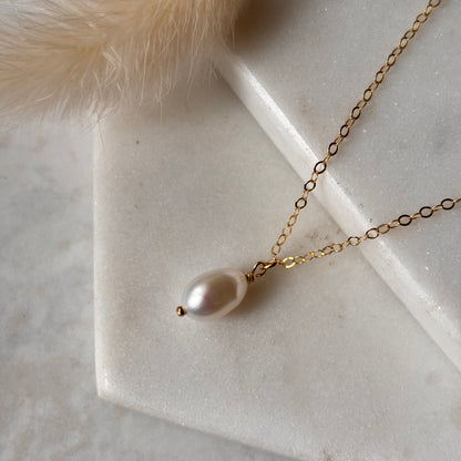 Gold necklace with a single pearl pendant on a marble surface