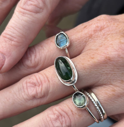 Close-up of a hand wearing multiple silver rings with green gemstones.