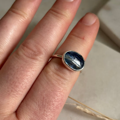 Hand wearing a silver ring with a blue stone on a neutral background