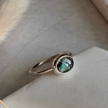 Silver ring with a green gemstone on a light stone surface