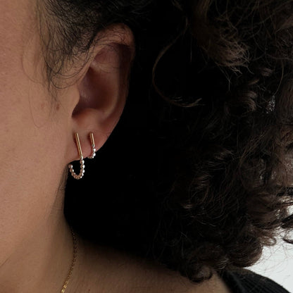 A set of two J-hoop earrings made of sterling silver with hand-textured orbs, worn by a model.