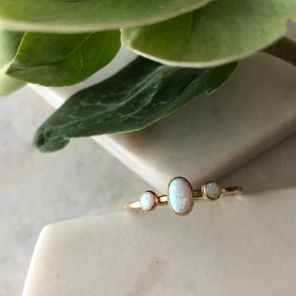 An oval triple gemstone ring with white opal set in gold, displayed on a marble surface.