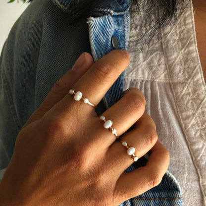 A hand wearing an oval triple gemstone ring with white opal set in gold.
