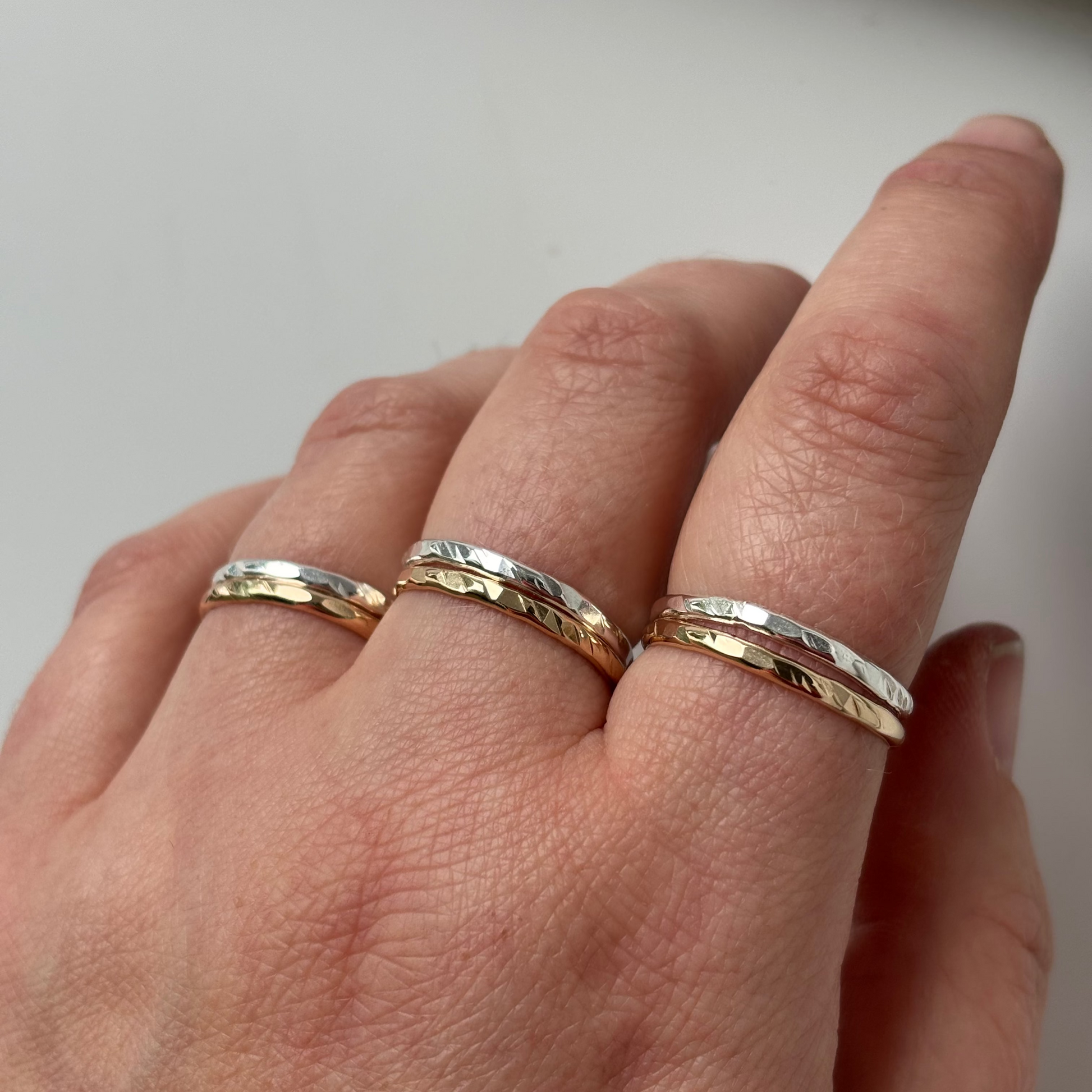 Three textured two-tone rings worn on a hand, featuring alternating bands of matte silver and hammered yellow gold.