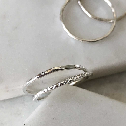 Two thin textured silver stacking bands on a white background.