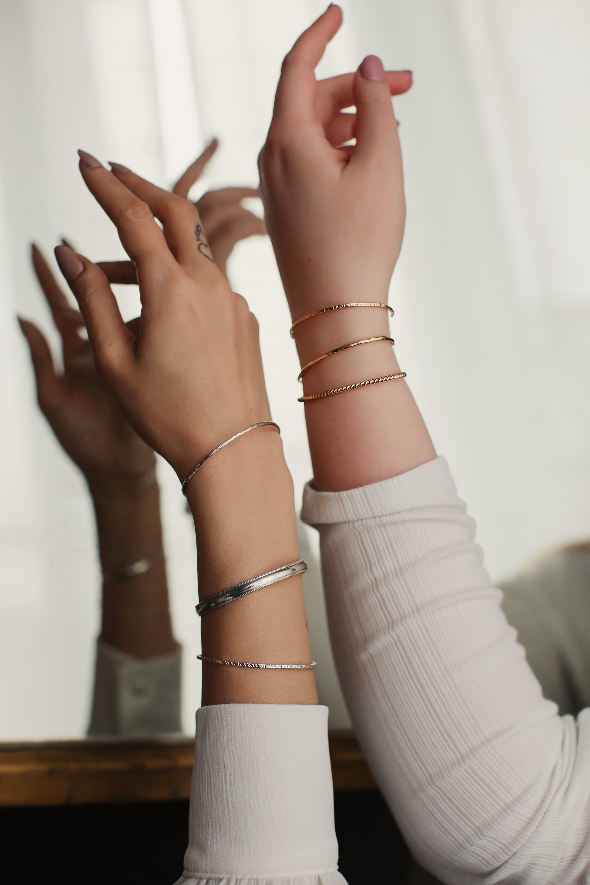 Close-up of hands wearing multiple bracelets on a neutral background