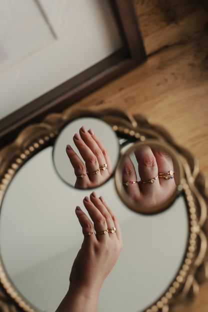 Hand wearing gold rings with a mirror reflection on a wooden floor.