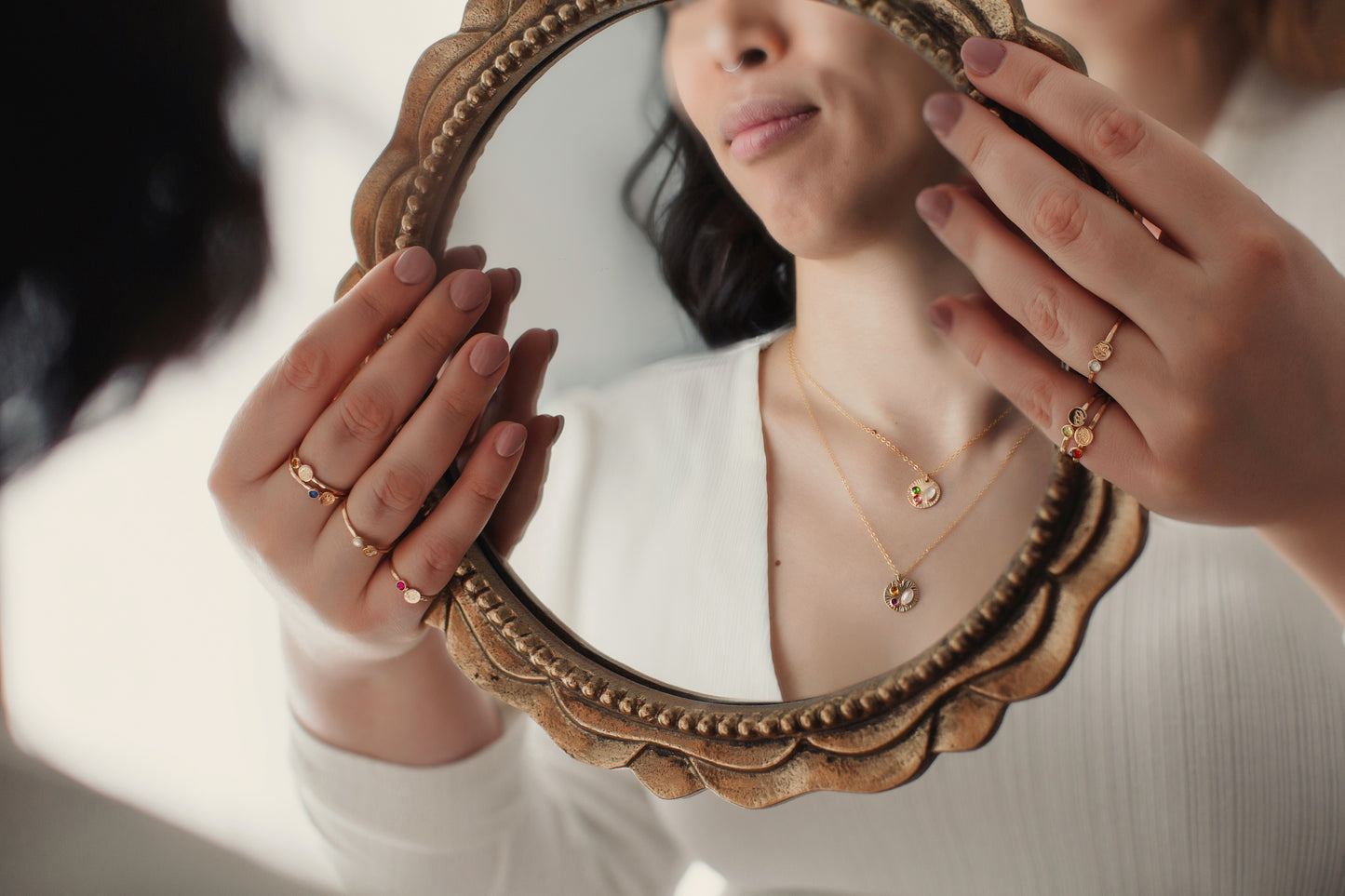 Person holding a decorative mirror with reflection showing jewelry.