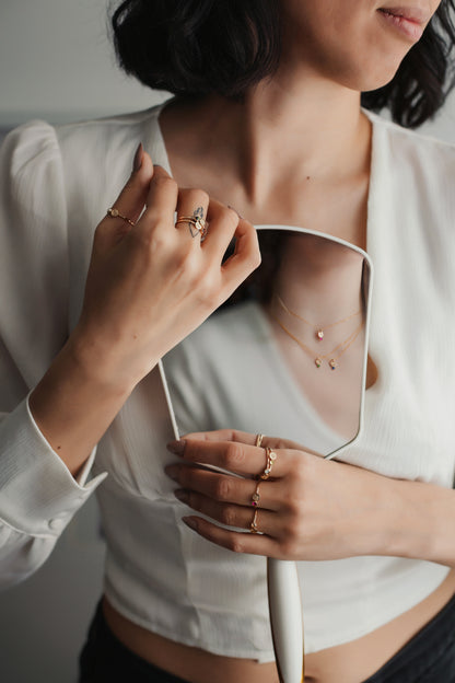 Person wearing a white shirt with a necklace, holding a mirror to check their reflection.