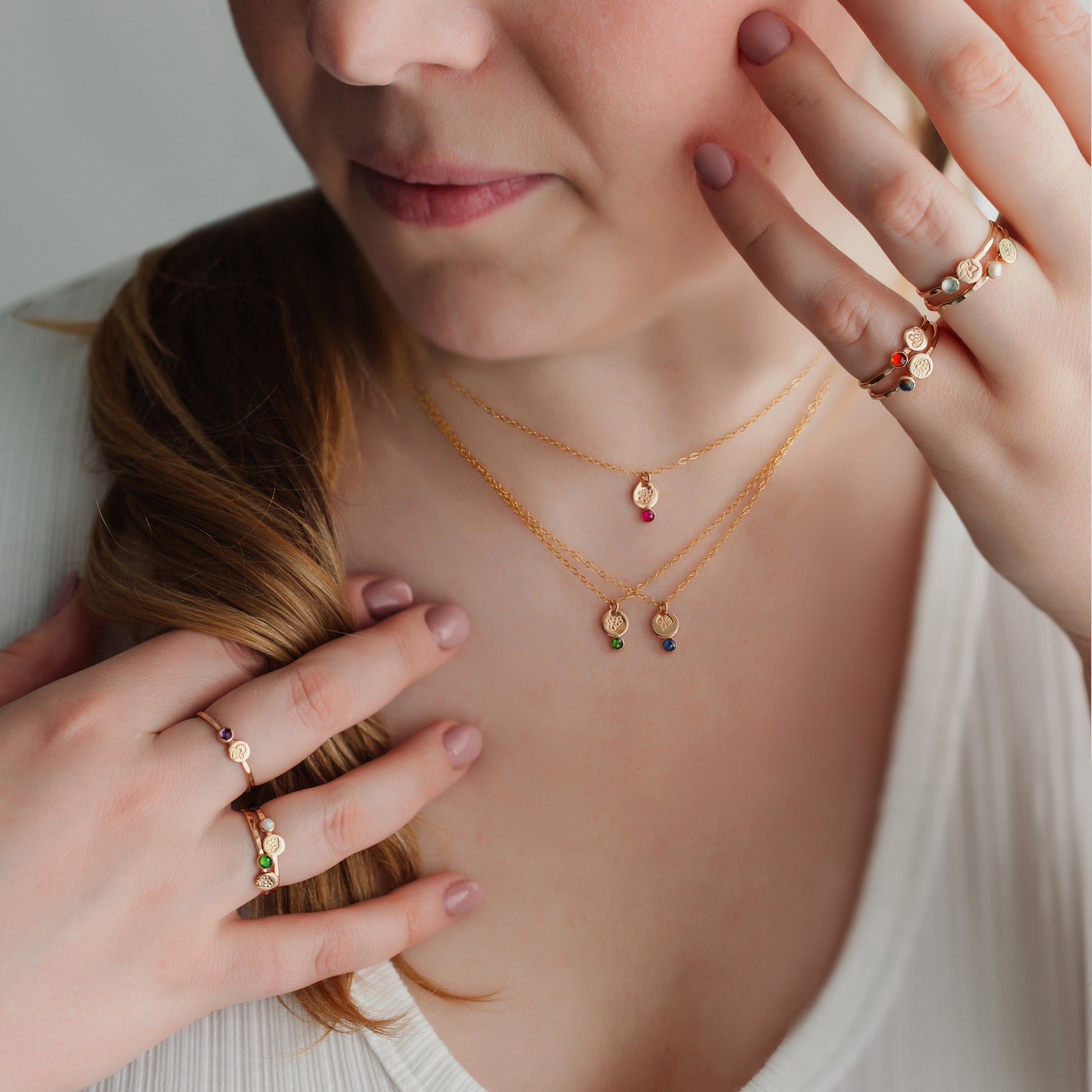 Woman wearing gold necklaces and rings, with a neutral background