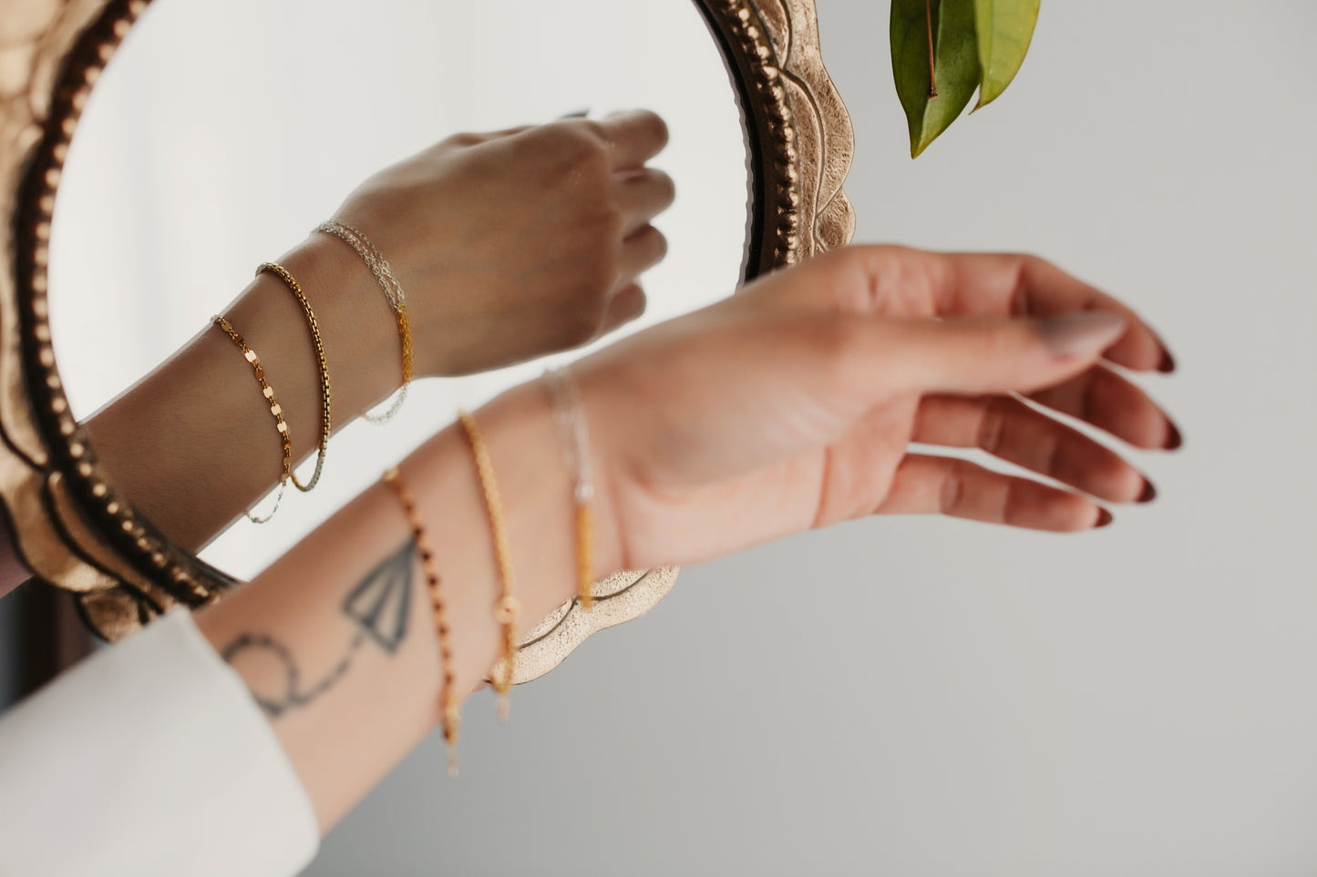 Close-up of hands with gold bracelets and a tattoo on a neutral background