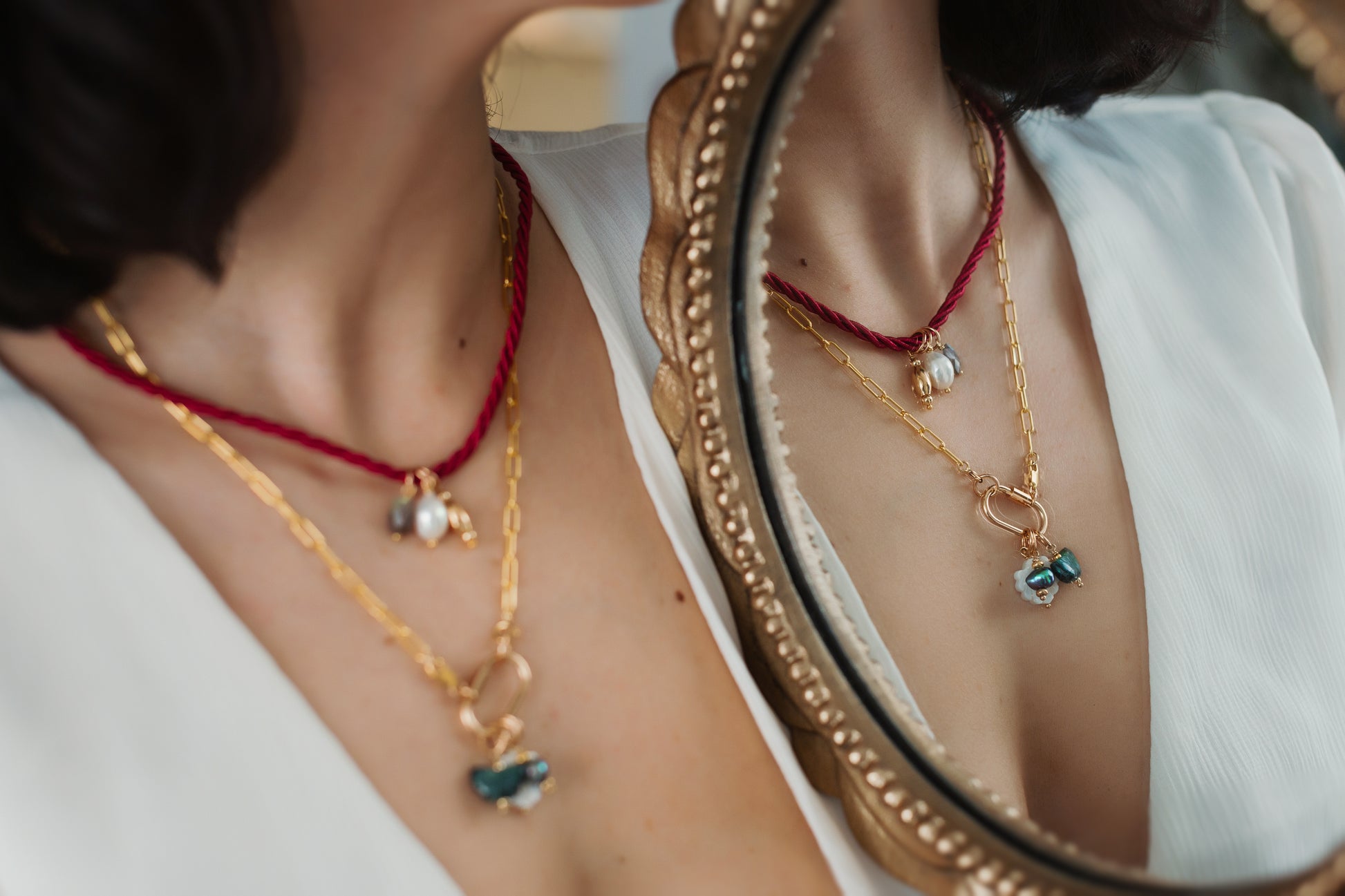 Person wearing a gold necklace with red cord, reflected in a mirror.