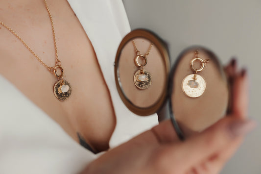 Close-up of a hand holding two gold necklaces with circular pendants.