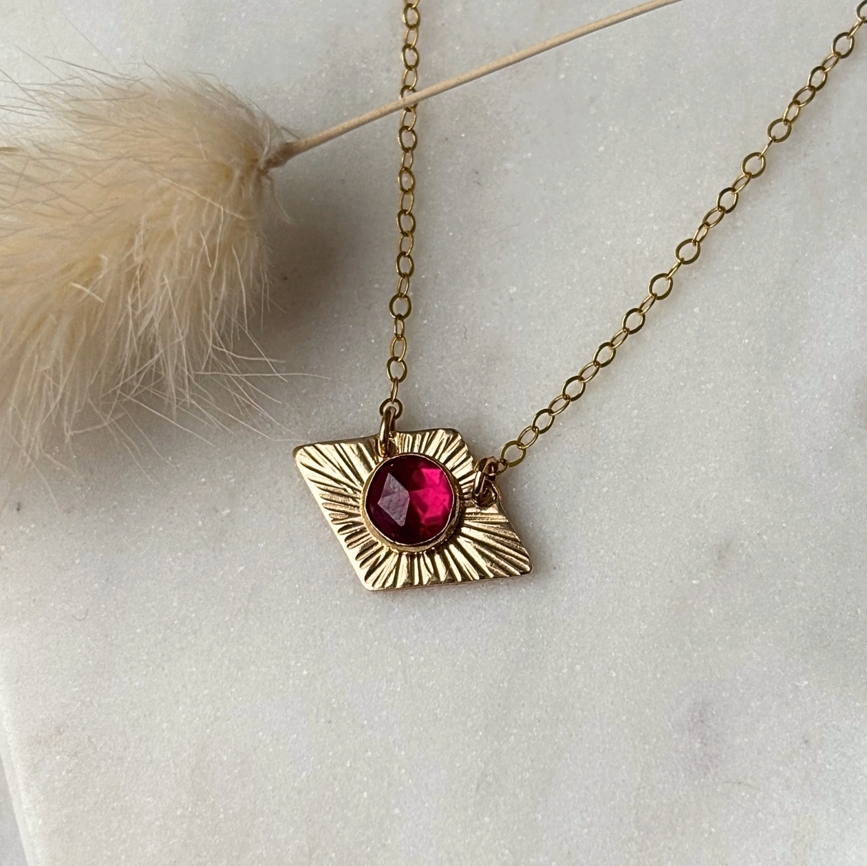 Gold necklace with a red gemstone pendant on a light background