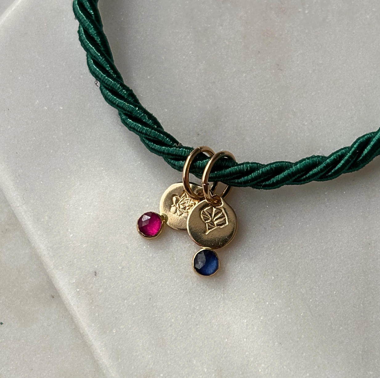 Green cord necklace with gold charms and gemstones on a light gray surface