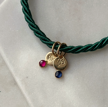 Green cord necklace with gold charms and gemstones on a light gray surface