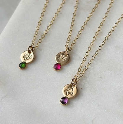 Three gold necklaces with gemstone pendants on a light gray surface