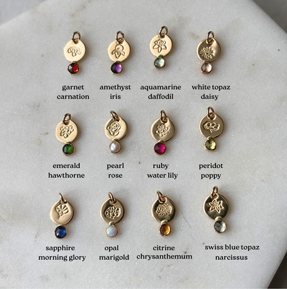 Collection of gold charms with gemstones and corresponding birthstone names on a marble surface