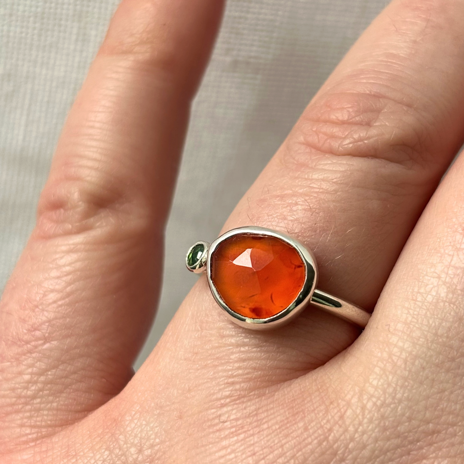silver ring with an orange gemstone on a finger