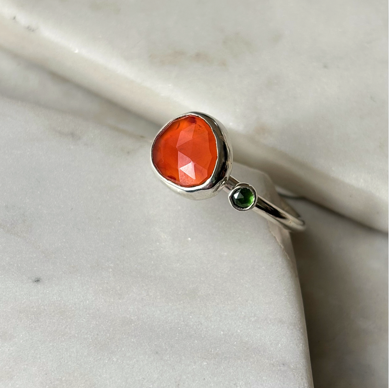 Silver ring with a orange stone on a marble surface