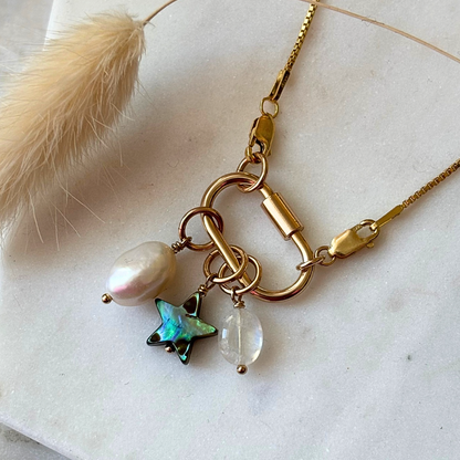 Gold necklace with a carabiner clip with star and pearl charm on a light background