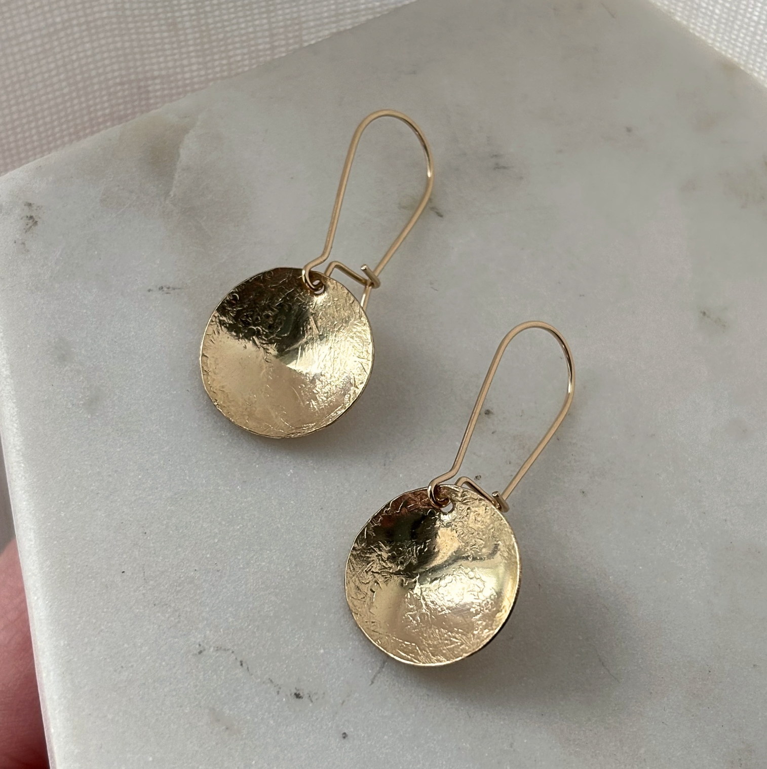 Gold disc earrings on a marble surface