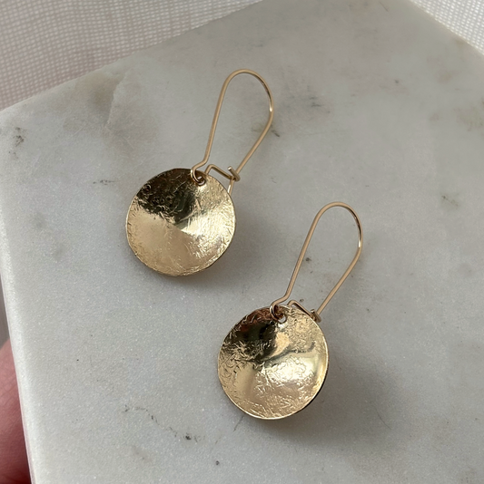 Gold disc earrings on a marble surface