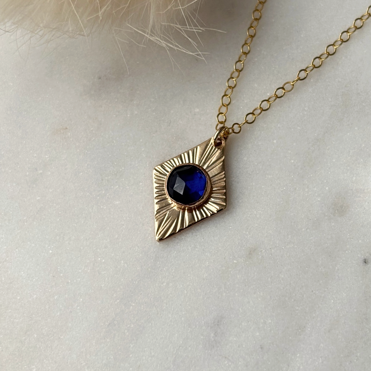 Gold necklace with a blue gemstone pendant on a light background
