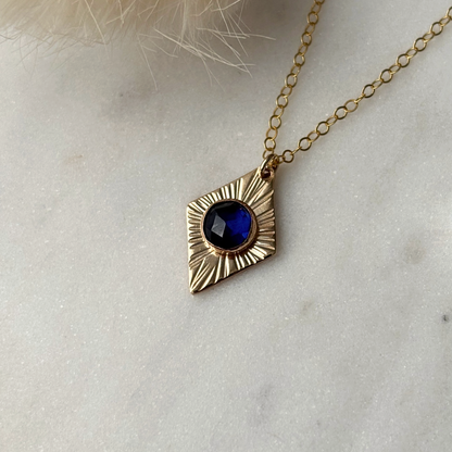 Gold necklace with a blue gemstone pendant on a light background