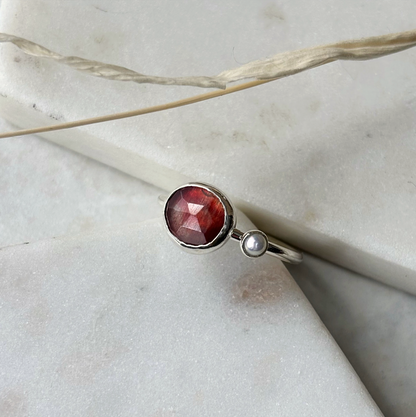 Silver ring with a red gemstone on a marble surface