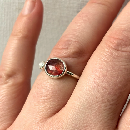 Silver ring with a red gemstone on a finger