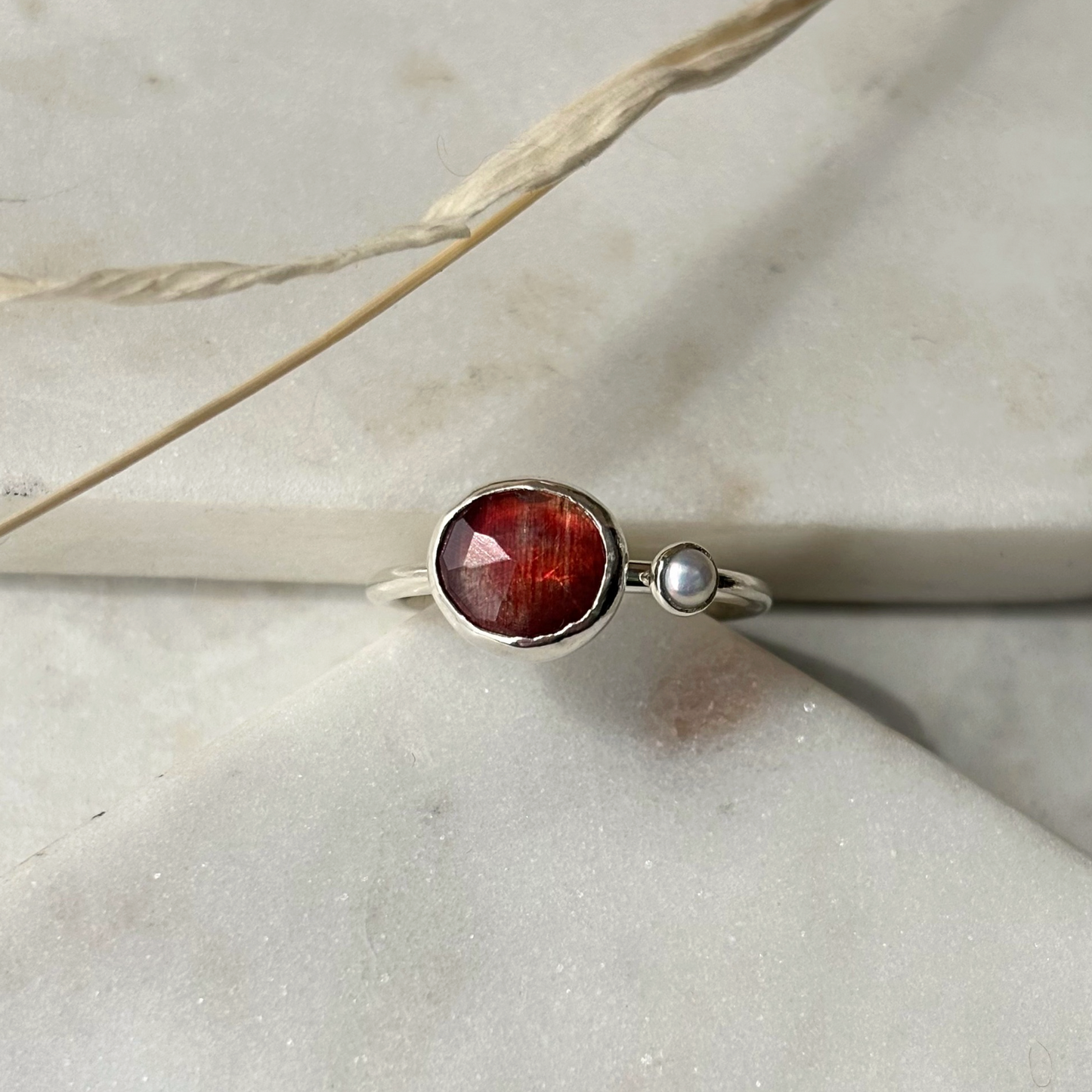 Silver ring with a red gemstone on a light stone surface