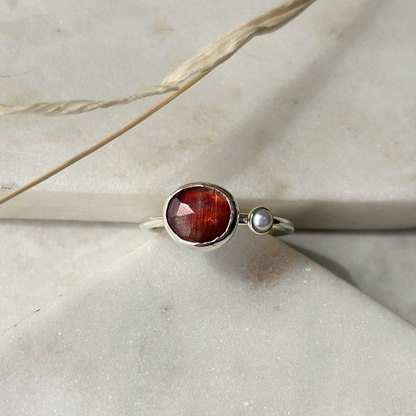 Silver ring with a red gemstone on a light stone surface