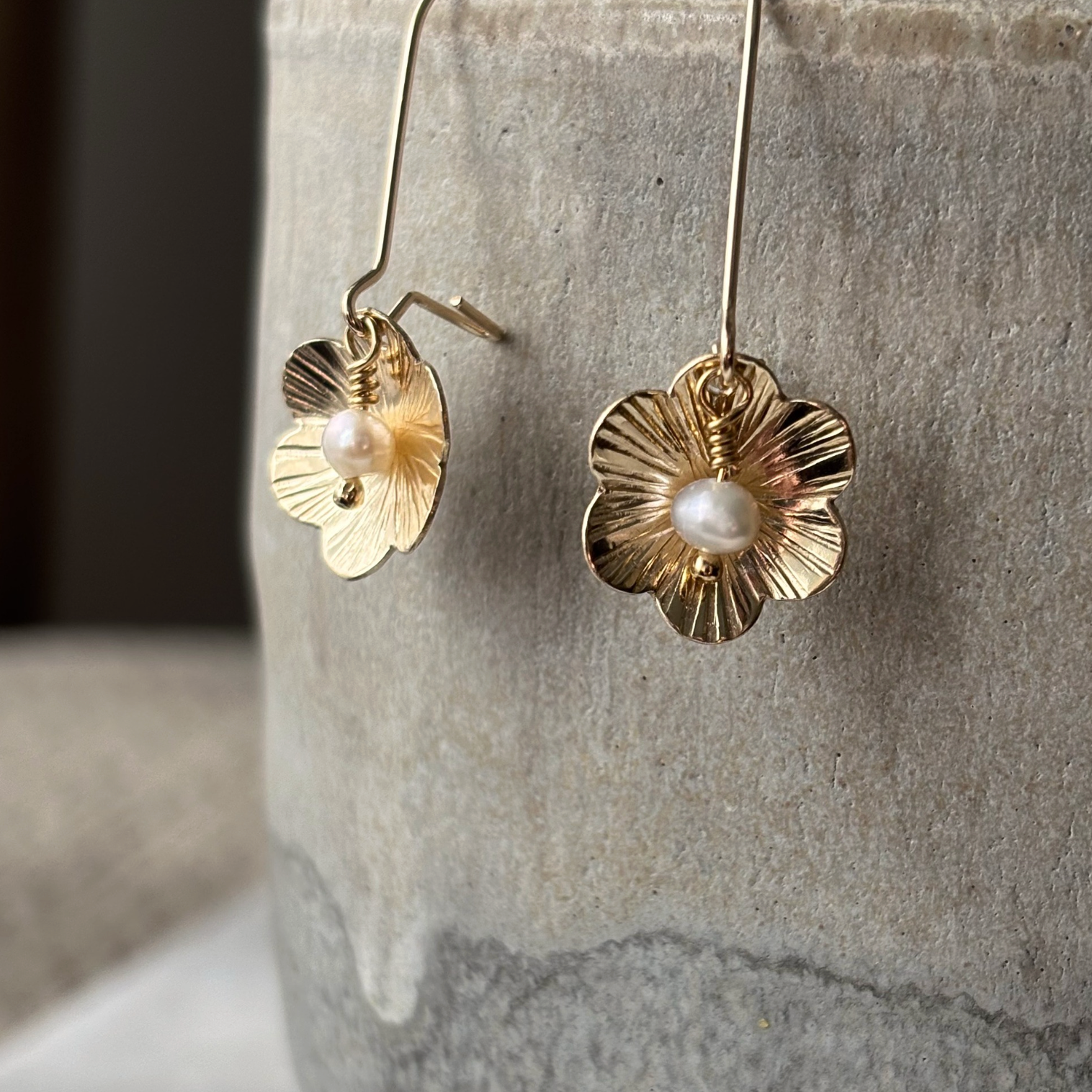 Gold floral earrings with pearl centers on a stone surface
