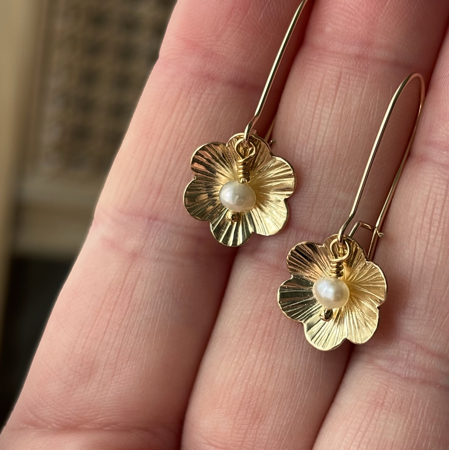 Gold flower-shaped earrings with pearl centers held between fingers.