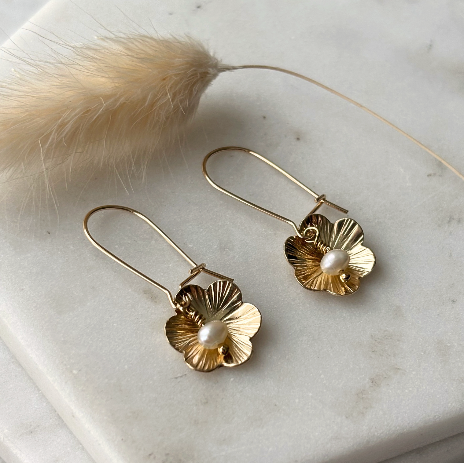 Gold floral earrings with pearl centers on a marble surface.