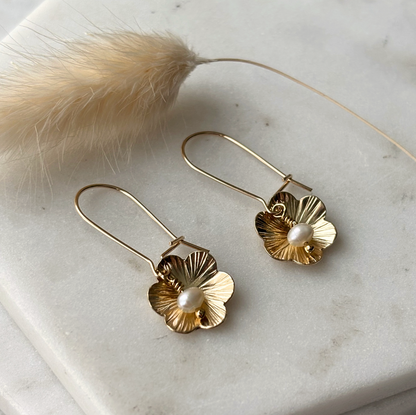 Gold floral earrings with pearl centers on a marble surface.