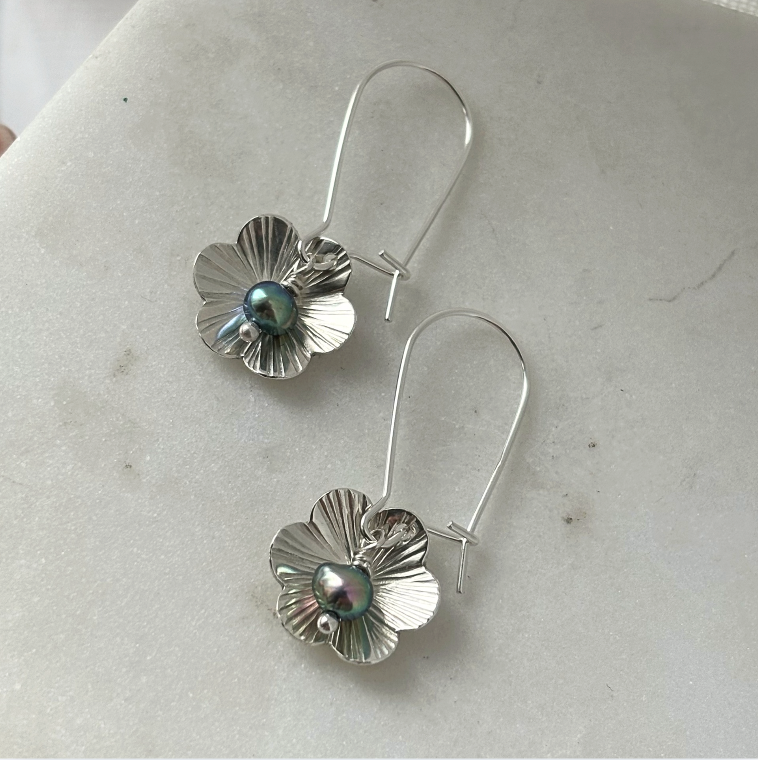 Silver flower-shaped earrings with a central pearl on a light gray surface