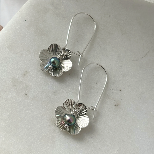Silver flower-shaped earrings with a central pearl on a light gray surface
